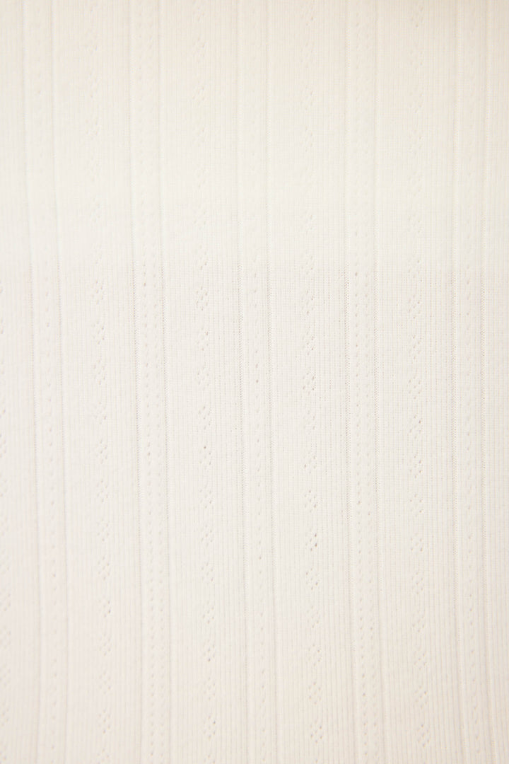 A close-up of P.J. Salvages Pointelle Essentials Solid Ivory Open Leg Pant shows off-white fabric with vertical textured stripes and evenly spaced eyelet patterns.