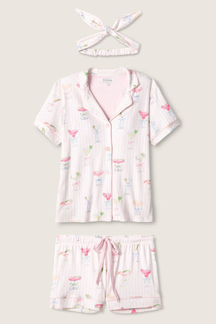 The P.J. Salvage Pretty Punch Cocktail Print 3-Piece Short Set features a short-sleeve button-up top, drawstring shorts, and a matching headband in light pink with colorful cocktail-themed prints.
