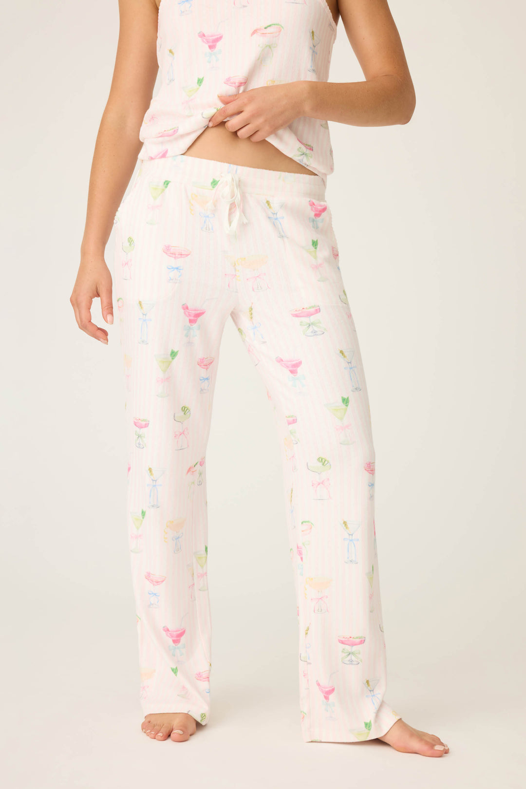 Someone stands barefoot against a plain background wearing P.J. Salvage Pretty Punch Cocktail Print Open Leg Pants—light-colored pajama pants with a drawstring waist and pastel cocktail glass patterns. The matching top is partially visible.