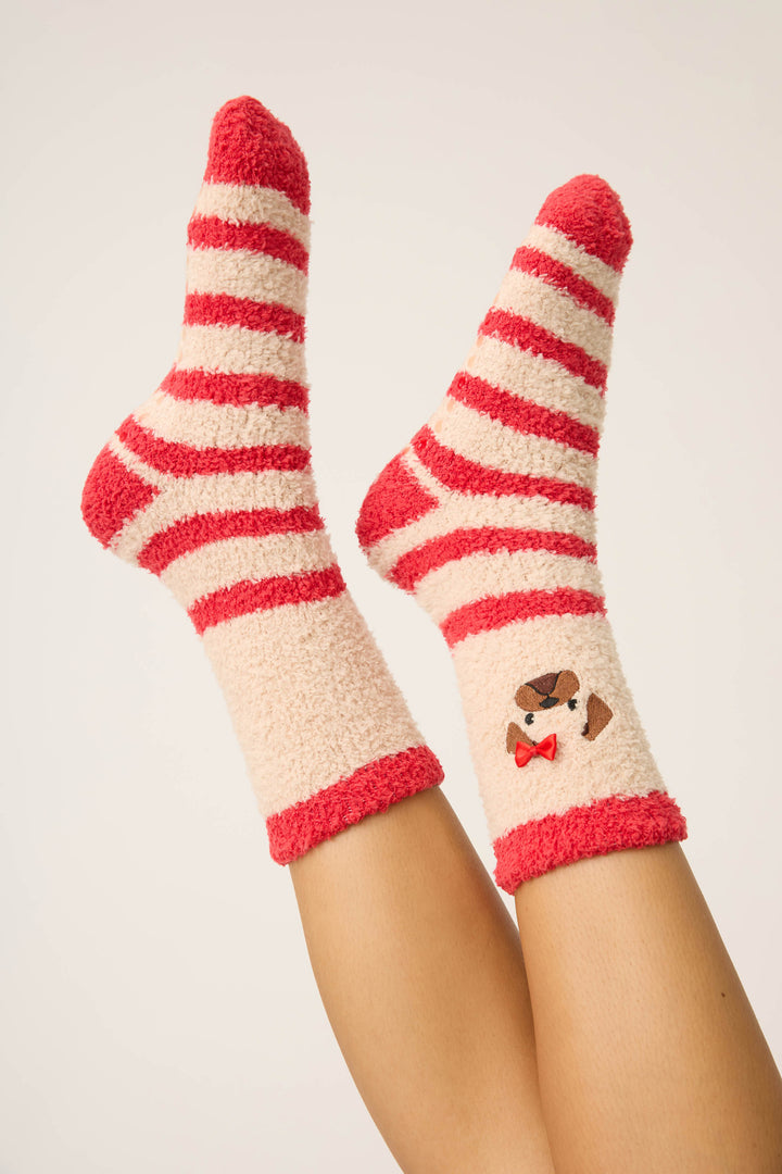 Two feet in P.J. Salvage Striped Dog Fuzzy Crew Socks—cream and red stripes, with one sock displaying an embroidered brown and white dog with a red bow tie. Legs are raised against an off-white background.