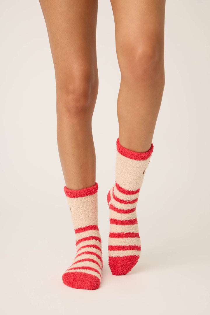 A person stands on a light background wearing P.J. Salvage Striped Dog Fuzzy Crew Socks in red and cream. The mid-calf socks are visible on their lower legs and feet.