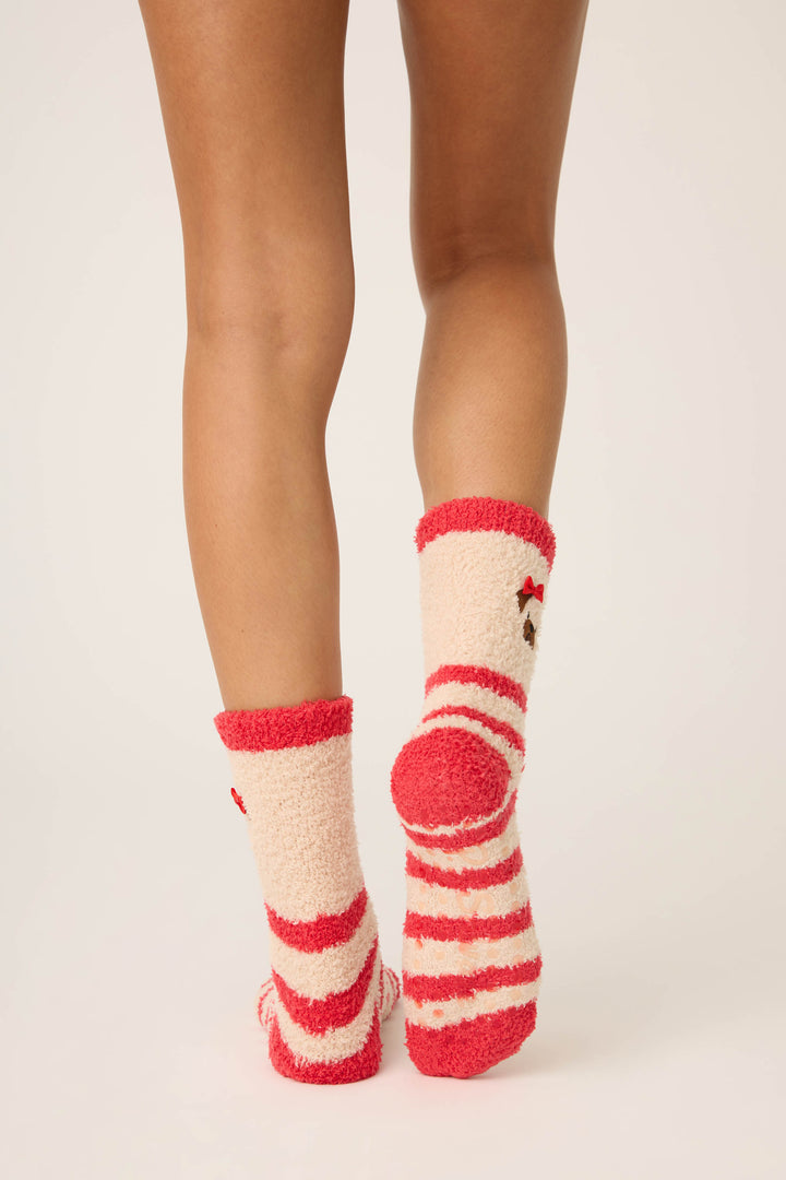 A person stands with bare legs, wearing P.J. Salvage Striped Dog Fuzzy Crew Socks with red and cream stripes and a small dog face design. The background is plain and light-colored.