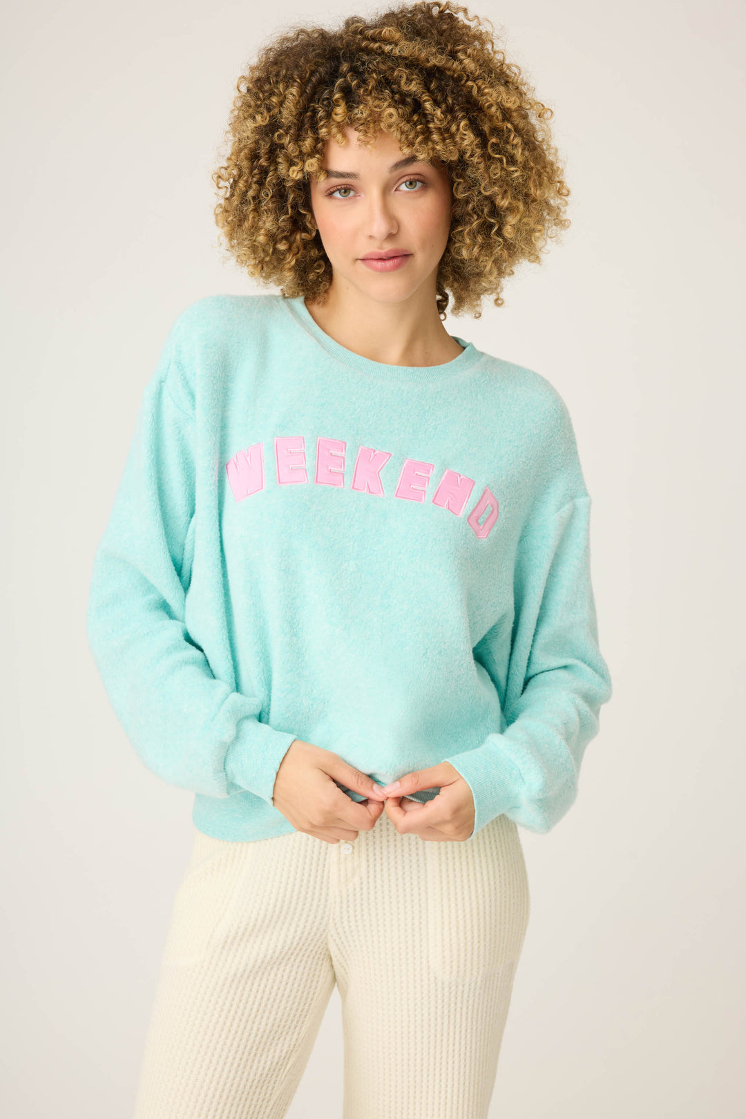 A person with curly hair wears the P.J. Salvage Secret Garden Weekend Graphic Sweatshirt in light blue and cream textured pants, standing against a plain light background.