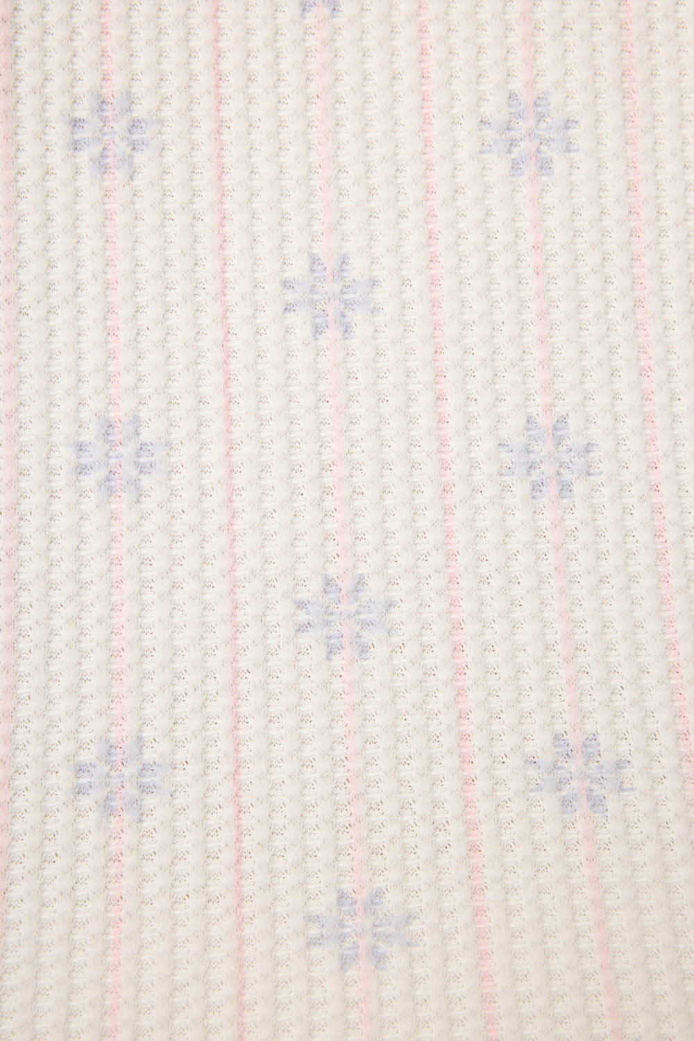 A close-up of the P.J. Salvage Ski Jammie Classics Snowflake Print PJ Set shows a white fabric with vertical pink grid lines and small blue snowflake shapes evenly patterned across the surface.