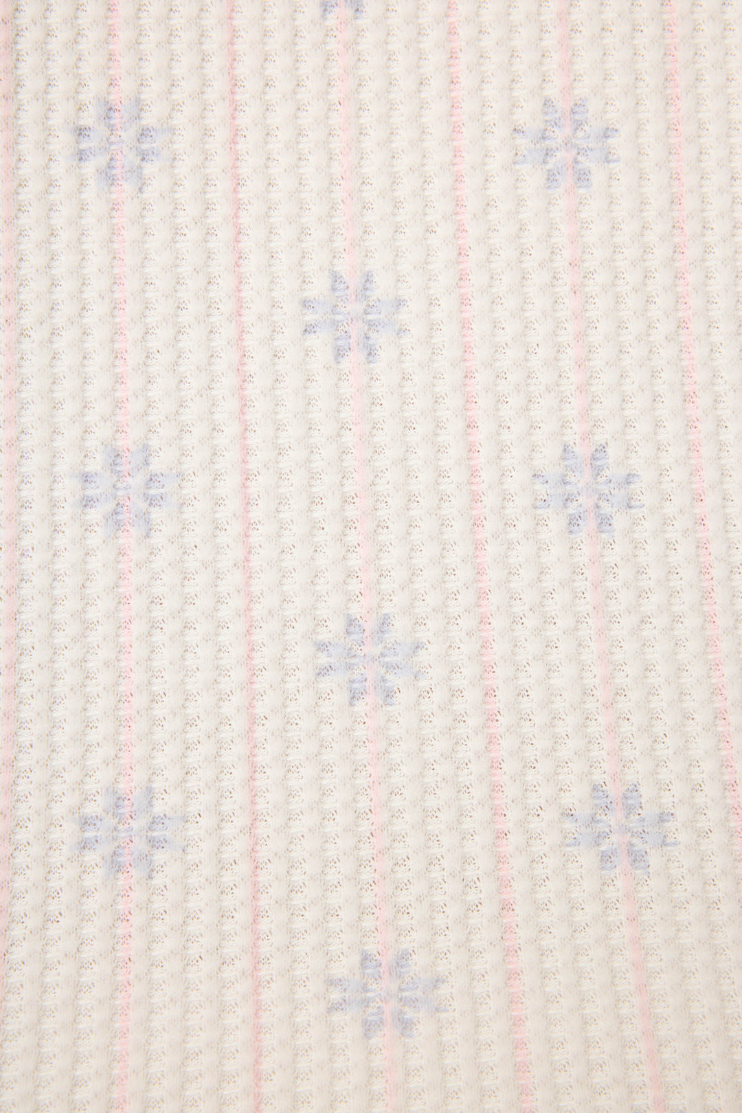 A close-up of the P.J. Salvage Ski Jammie Classics Snowflake Print PJ Set shows a white fabric with vertical pink grid lines and small blue snowflake shapes evenly patterned across the surface.