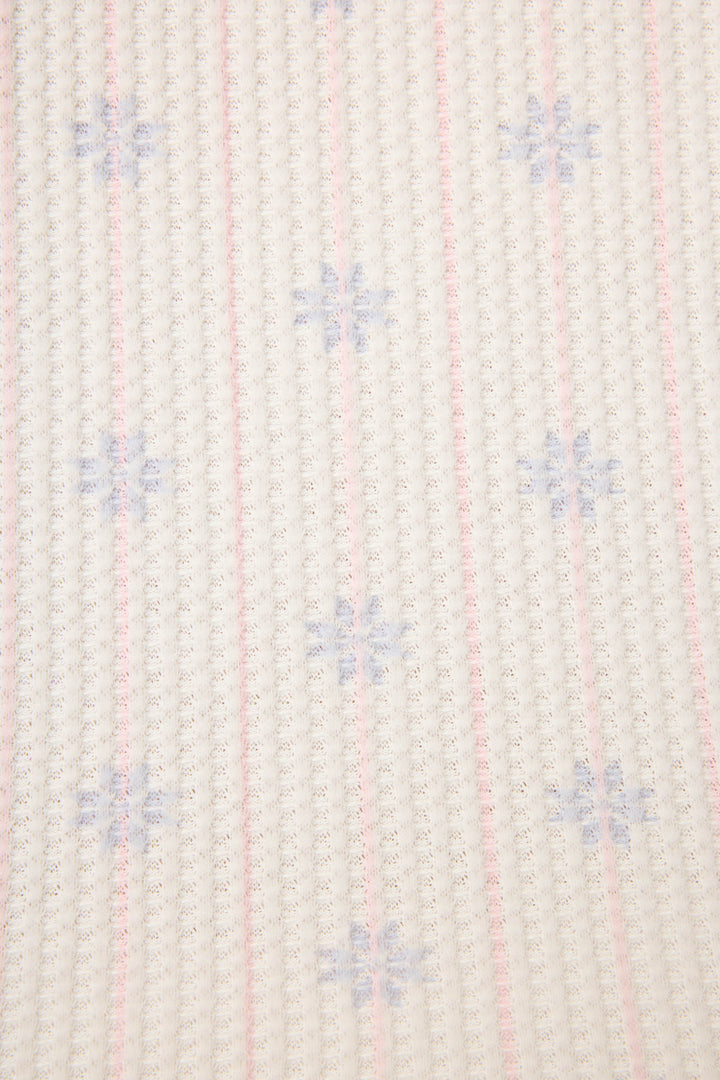 A close-up of the P.J. Salvage Ski Jammie Classics Snowflake Print PJ Set shows a white fabric with vertical pink grid lines and small blue snowflake shapes evenly patterned across the surface.