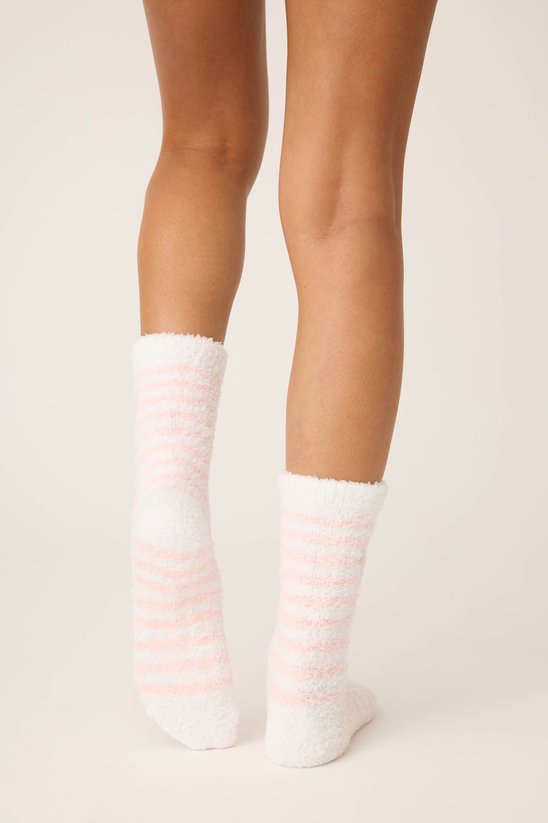 A person is shown from the knees down on a light background, wearing P.J. Salvage Striped Snowflake Fuzzy Crew Socks in white with light pink stripes.