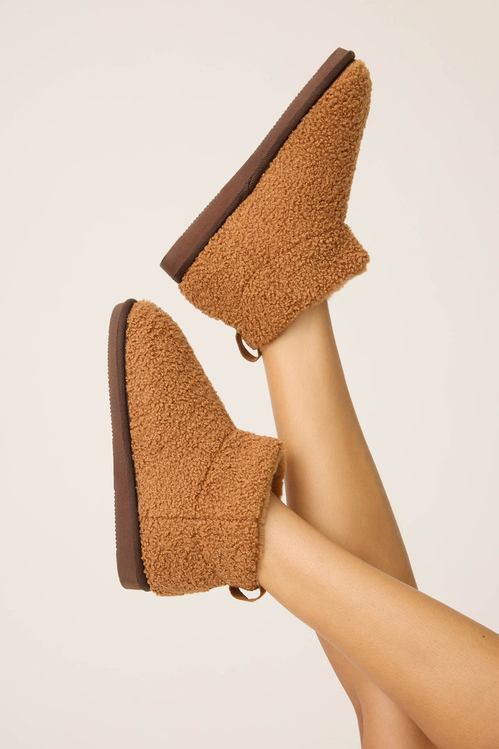 A person’s legs are raised in the air, showing P.J. Salvage Teddy Bear Sherpa Booties with dark brown soles, set against a plain light background.
