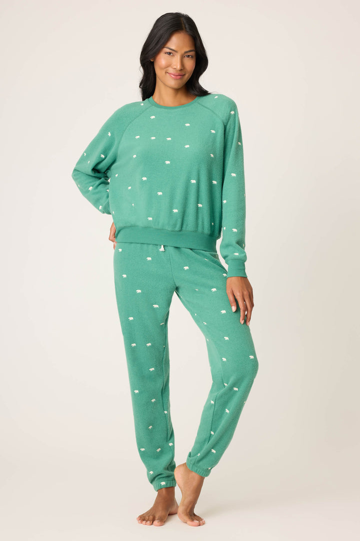 A person stands barefoot in a P.J. Salvage The Outsider Embroidered Bear Fleece Sweatshirt with matching pants, both featuring small white dots, against a plain light background.