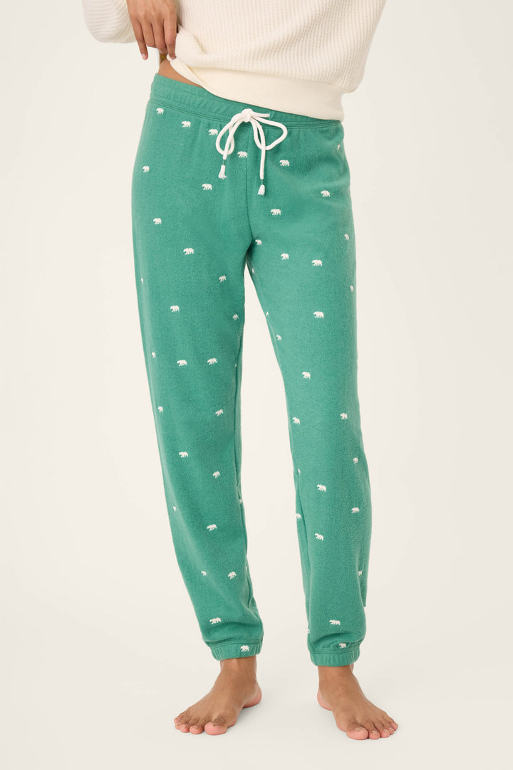 Wearing P.J. Salvage’s The Outsider Embroidered Bear Fleece Banded Pants in green with a small white print and a cream sweater, a person stands barefoot against a plain background, face not visible.