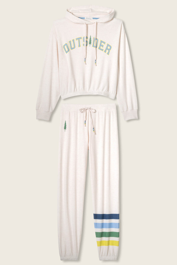 The Outsider Graphic Jogger Lounge Set by P.J. Salvage includes a cream hooded sweatshirt with “OUTSIDER” in green and yellow, plus joggers featuring a tree graphic and green, blue, and yellow stripes at the hem.