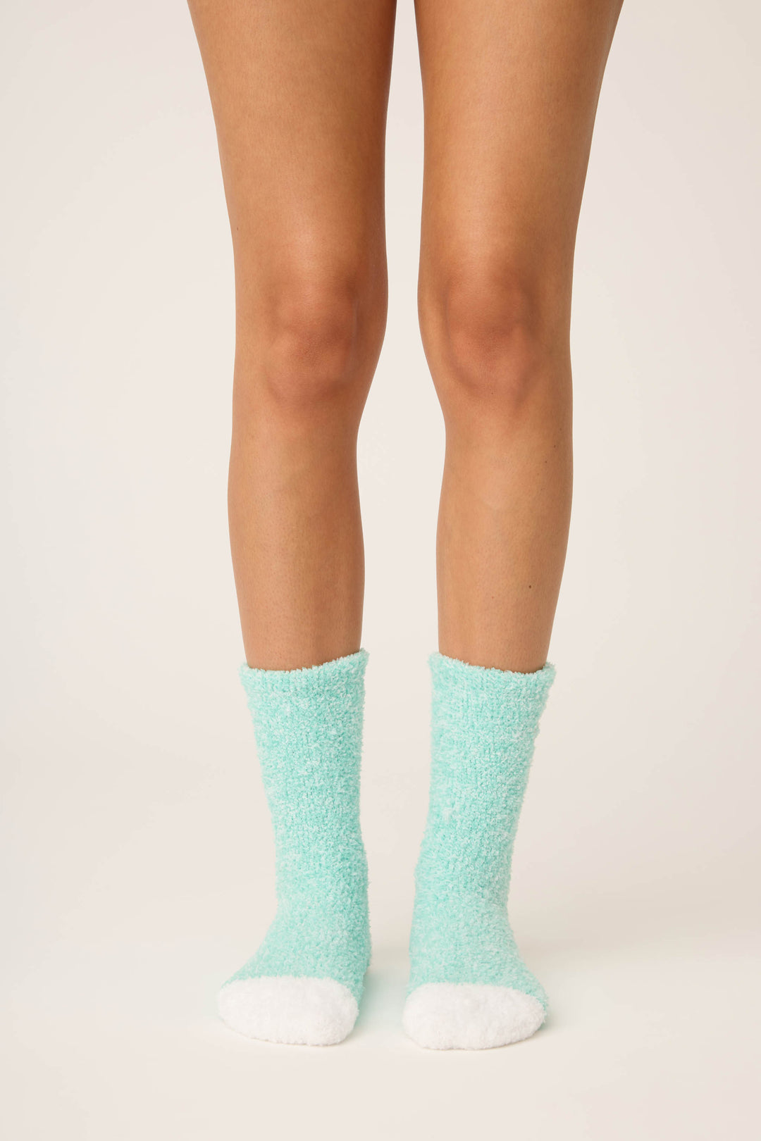 A person stands on a light surface wearing P.J. Salvage Candy Cane Fuzzy Crew Socks. Only their legs and feet, in these cozy socks, are visible against a plain background.
