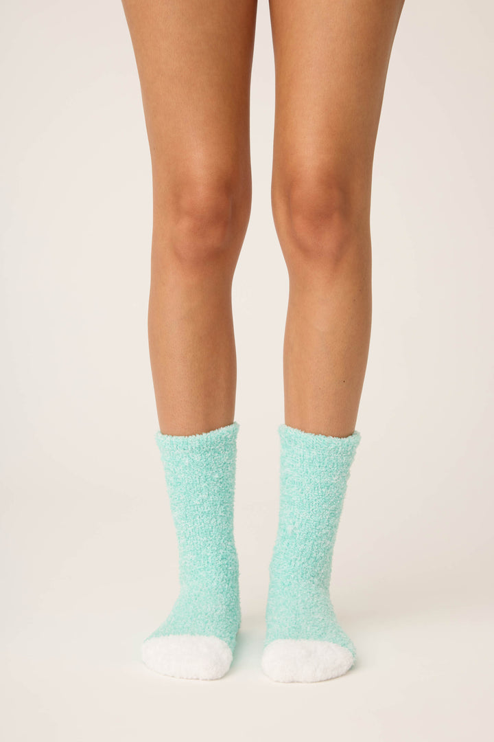 A person stands on a light surface wearing P.J. Salvage Candy Cane Fuzzy Crew Socks. Only their legs and feet, in these cozy socks, are visible against a plain background.