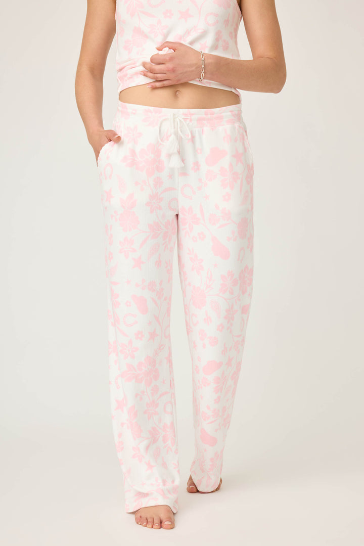 A person wears P.J. Salvage Wild Flower Western Floral Print Open Leg Pants with a matching tank top and bracelet. One hand is in a pocket, the other on their stomach, and they're barefoot.