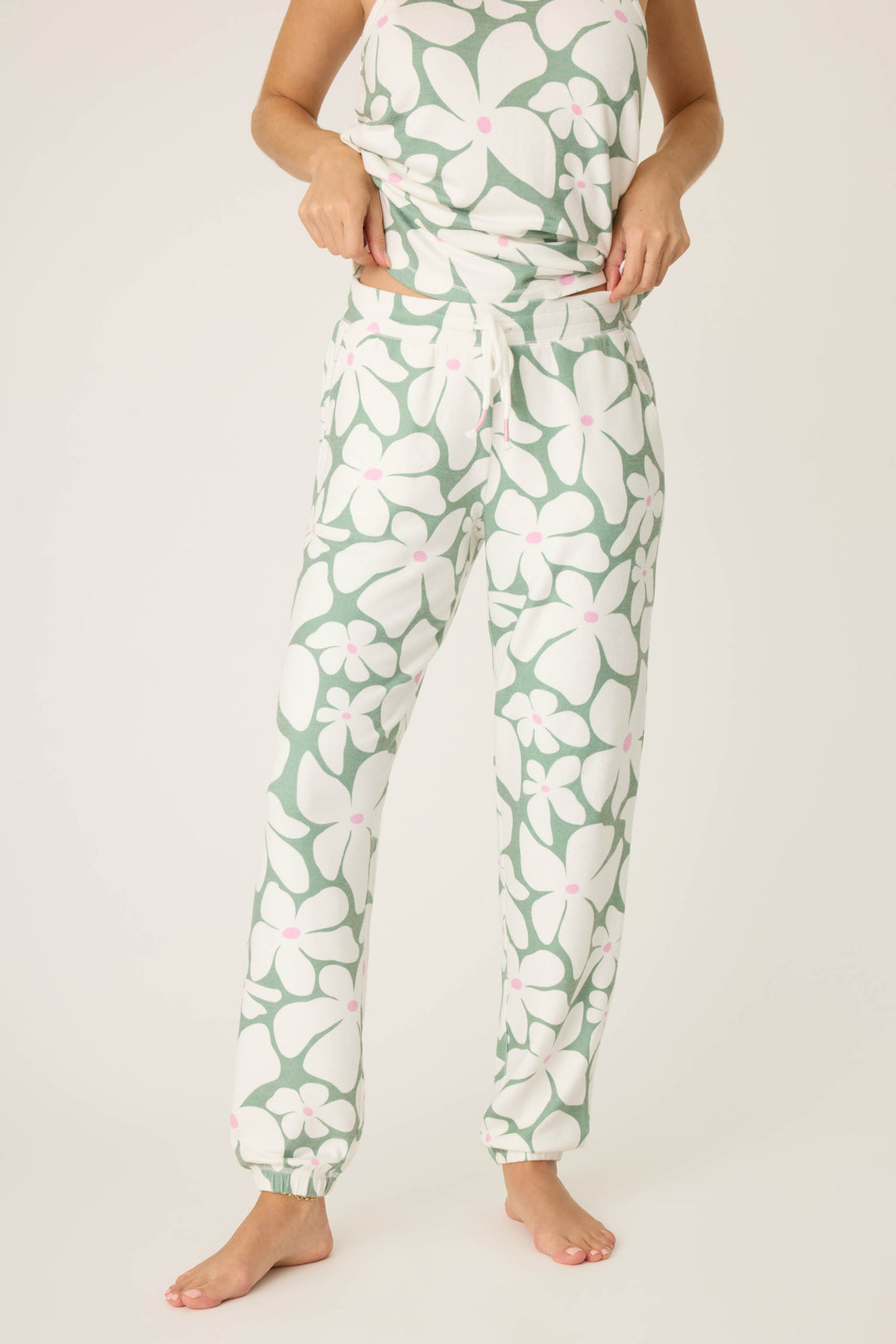 A model, head not shown, stands barefoot on a light background wearing P.J. Salvage's Wish You Were Here Floral Print Banded Pants with a matching green, white, and pink floral top.