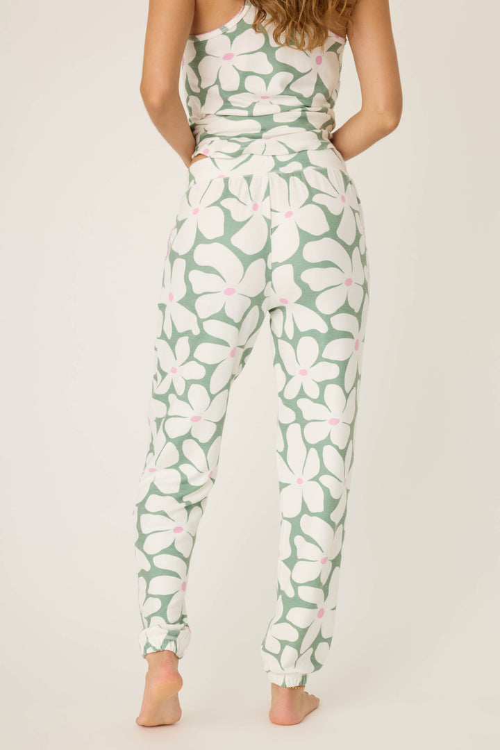 A person faces away, barefoot, modeling P.J. Salvage's Wish You Were Here Floral Print Banded Pants—light green with large white flowers and pink dots. Only their upper back, arms, and hair are visible.
