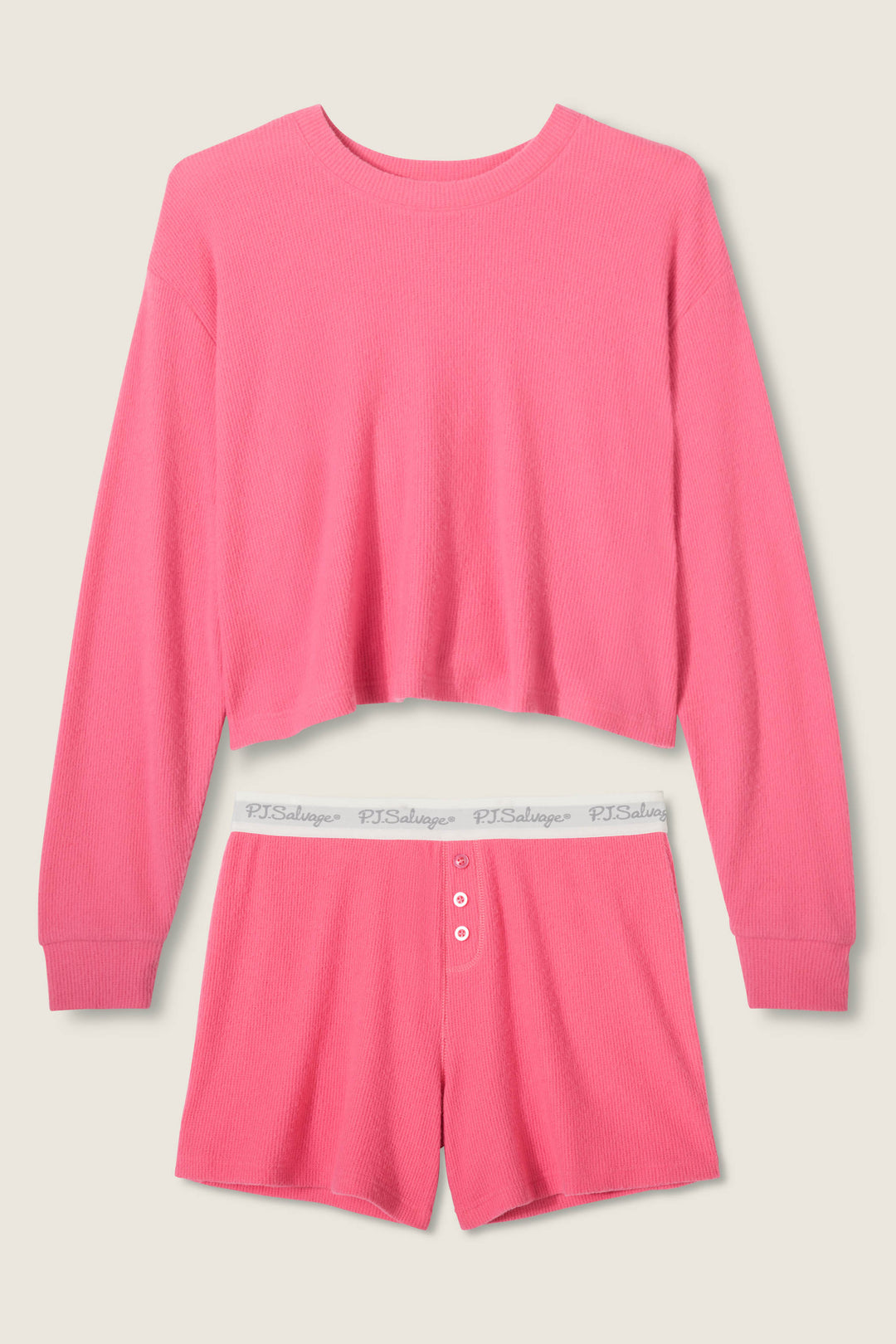 The P.J. Salvage Boyfriend Boxer Solid Pink Short Set features a long-sleeve cropped crewneck top and high-waisted shorts with a white elastic logo waistband and three-button front, set against a light beige background.