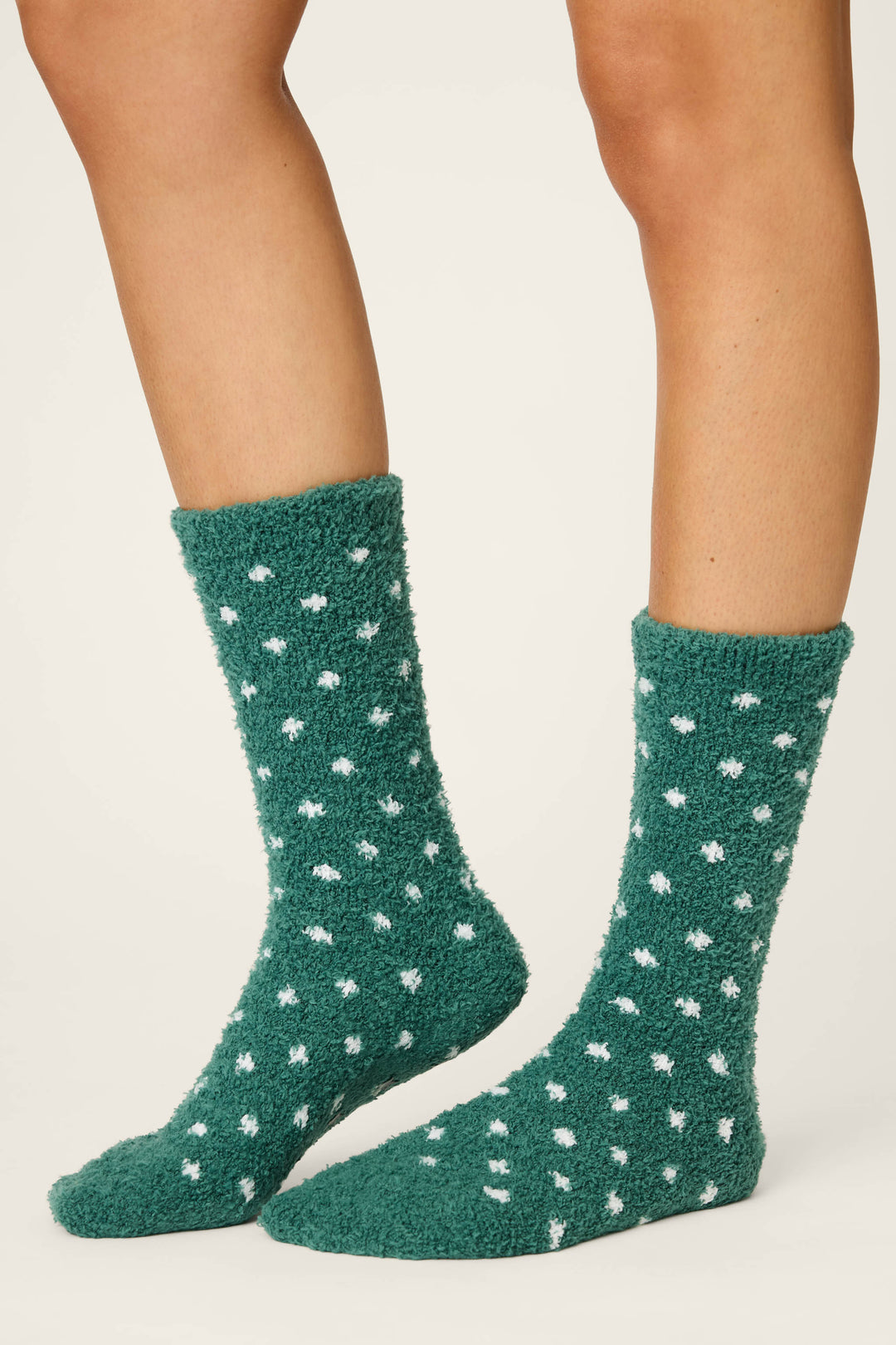 A person models P.J. Salvage’s DOTS SOCKS LET'S GET TOASTY—fuzzy green socks with white polka dots—standing on a neutral background, with only their lower legs and feet visible.