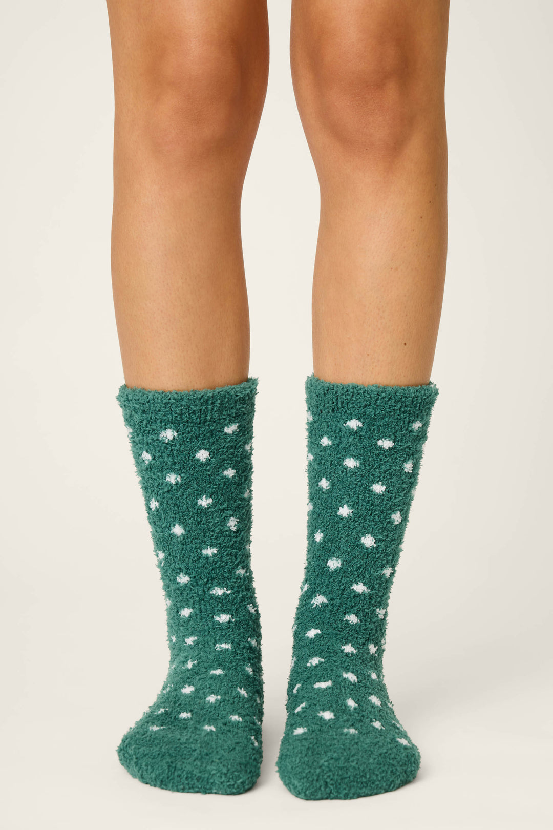 Only the lower legs and feet are visible as a person stands on a plain surface, wearing P.J. Salvage DOTS SOCKS LET'S GET TOASTY—fuzzy green socks with white polka dots.