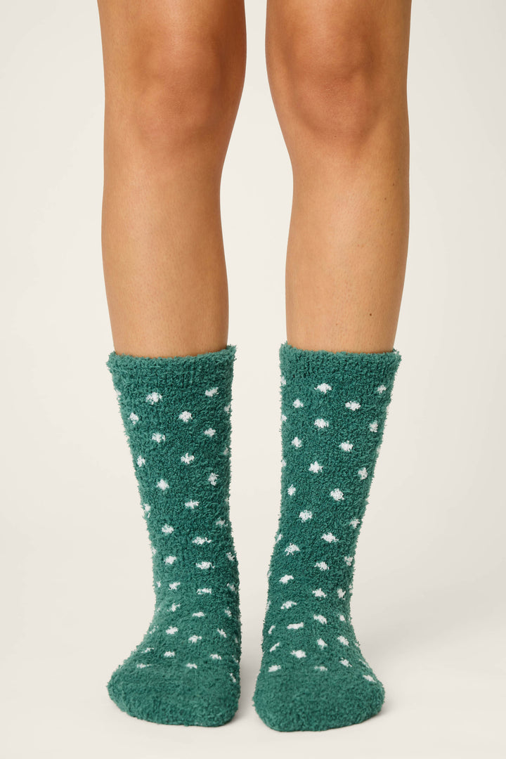 Only the lower legs and feet are visible as a person stands on a plain surface, wearing P.J. Salvage DOTS SOCKS LET'S GET TOASTY—fuzzy green socks with white polka dots.