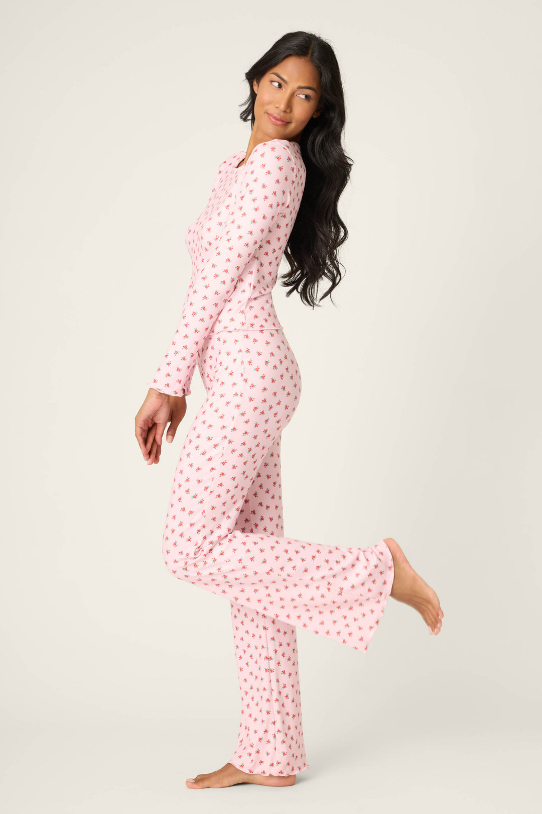 Woman in the P.J. Salvage Crazy For The Holidays Ditsy Floral Print Pants Set poses sideways, lifting one leg and looking over her shoulder—perfect cozy pajamas for girls’ holiday lounging against a plain light background.