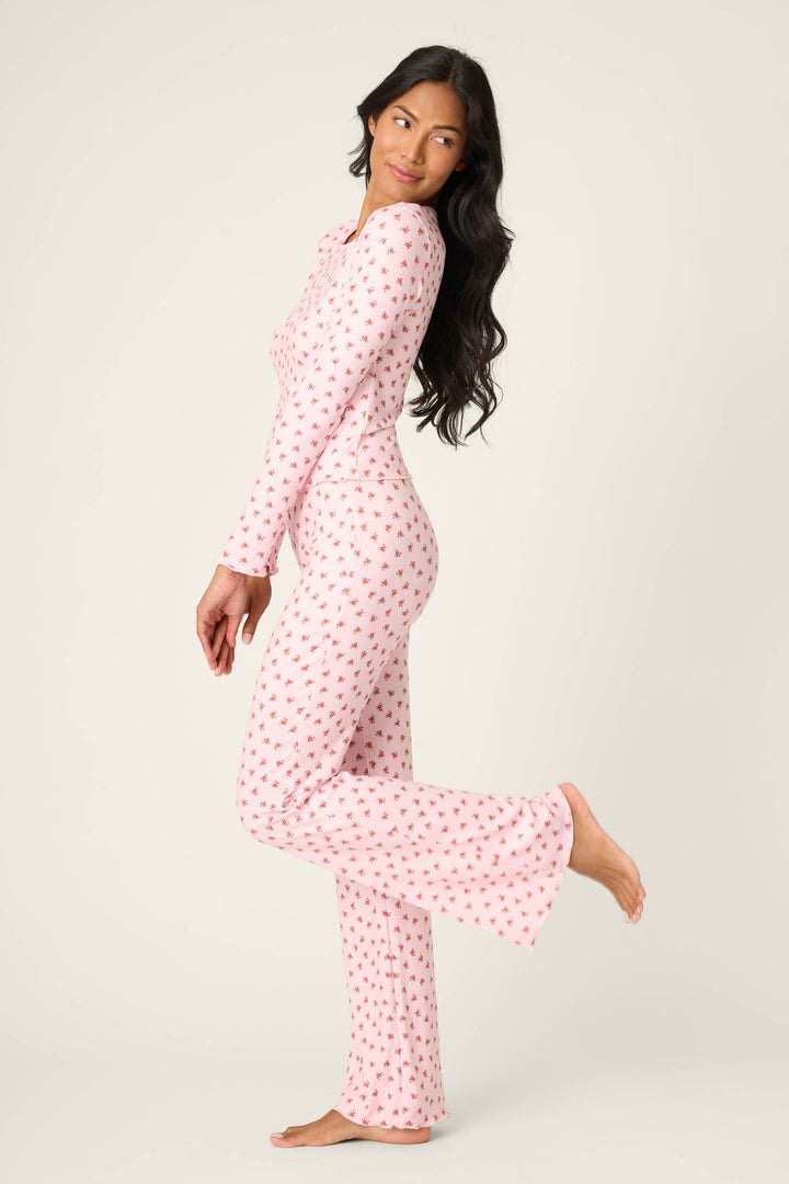 Woman in the P.J. Salvage Crazy For The Holidays Ditsy Floral Print Pants Set poses sideways, lifting one leg and looking over her shoulder—perfect cozy pajamas for girls’ holiday lounging against a plain light background.