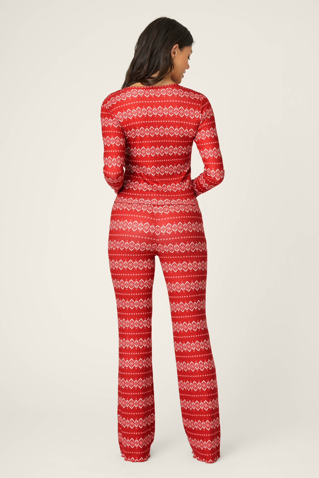 A woman faces away from the camera, wearing the P.J. Salvage Crazy For The Holidays Fairisle Print Pants Set. The plain light background highlights the festive pajama vibe of this red set with a classic Fair Isle motif.
