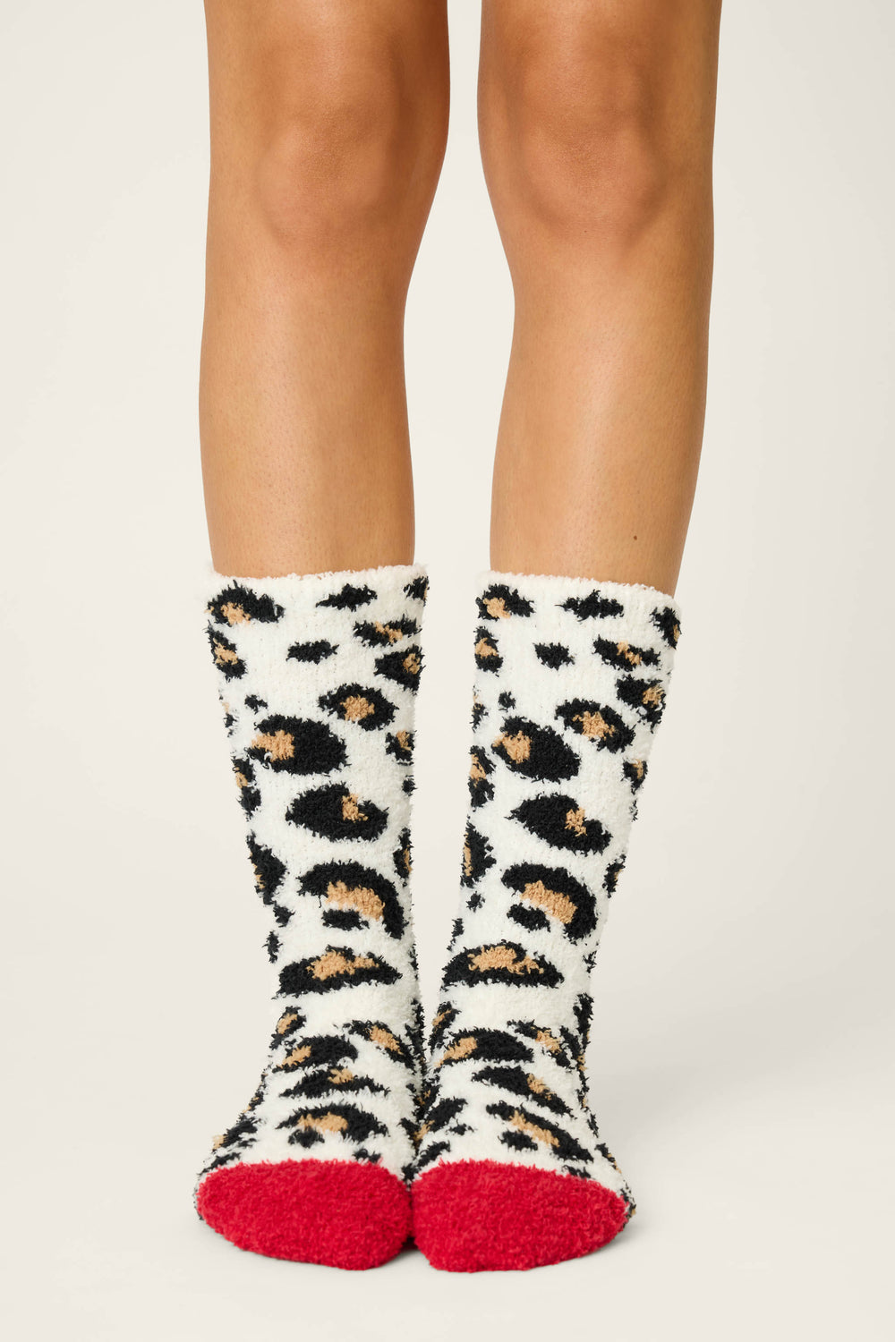 A person models P.J. Salvage LEOPARD SOCKS HOLIDAY DREAMS—cozy, fuzzy socks featuring a black, tan, and white leopard print with bright red toes—against a plain light background.