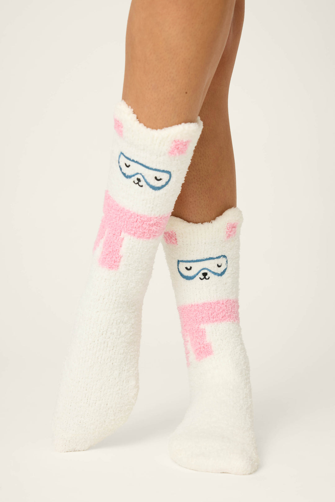Someone wears P.J. Salvage BEAR SOCKS FAM JAM BEARLY AWAKE—white fuzzy mid-calf socks with pink and blue cartoon bear faces and ears—against a plain, light background.