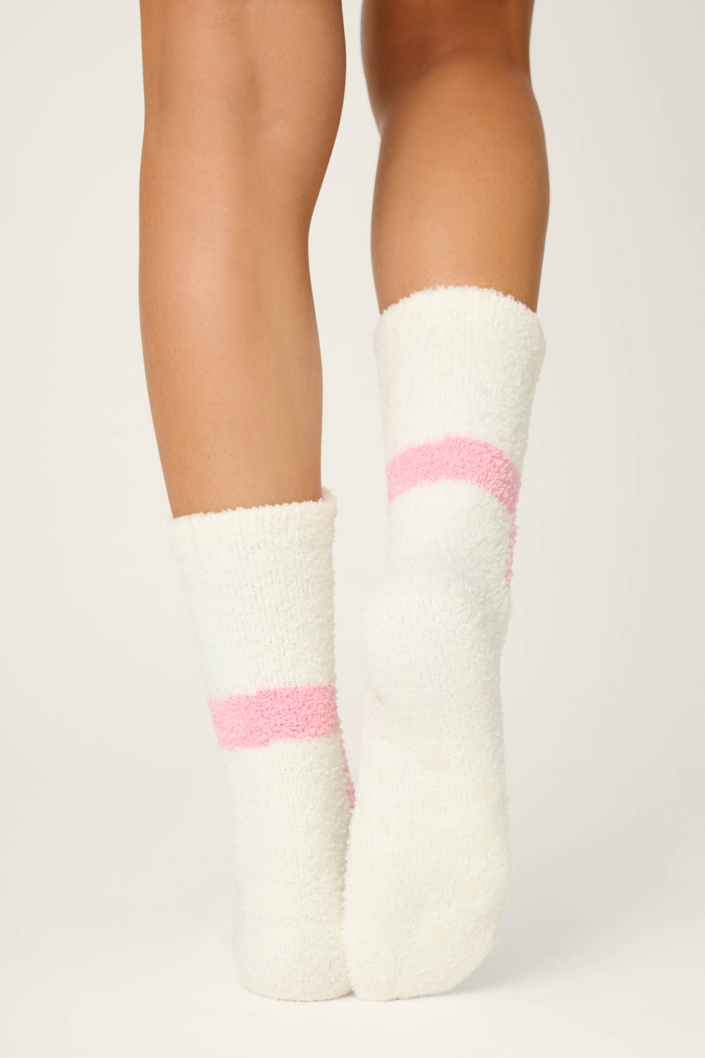 Close-up of a person's lower legs and feet wearing P.J. Salvage BEAR SOCKS FAM JAM BEARLY AWAKE fuzzy white socks with pink stripes, standing on a light surface with heels together and toes pointing outward.