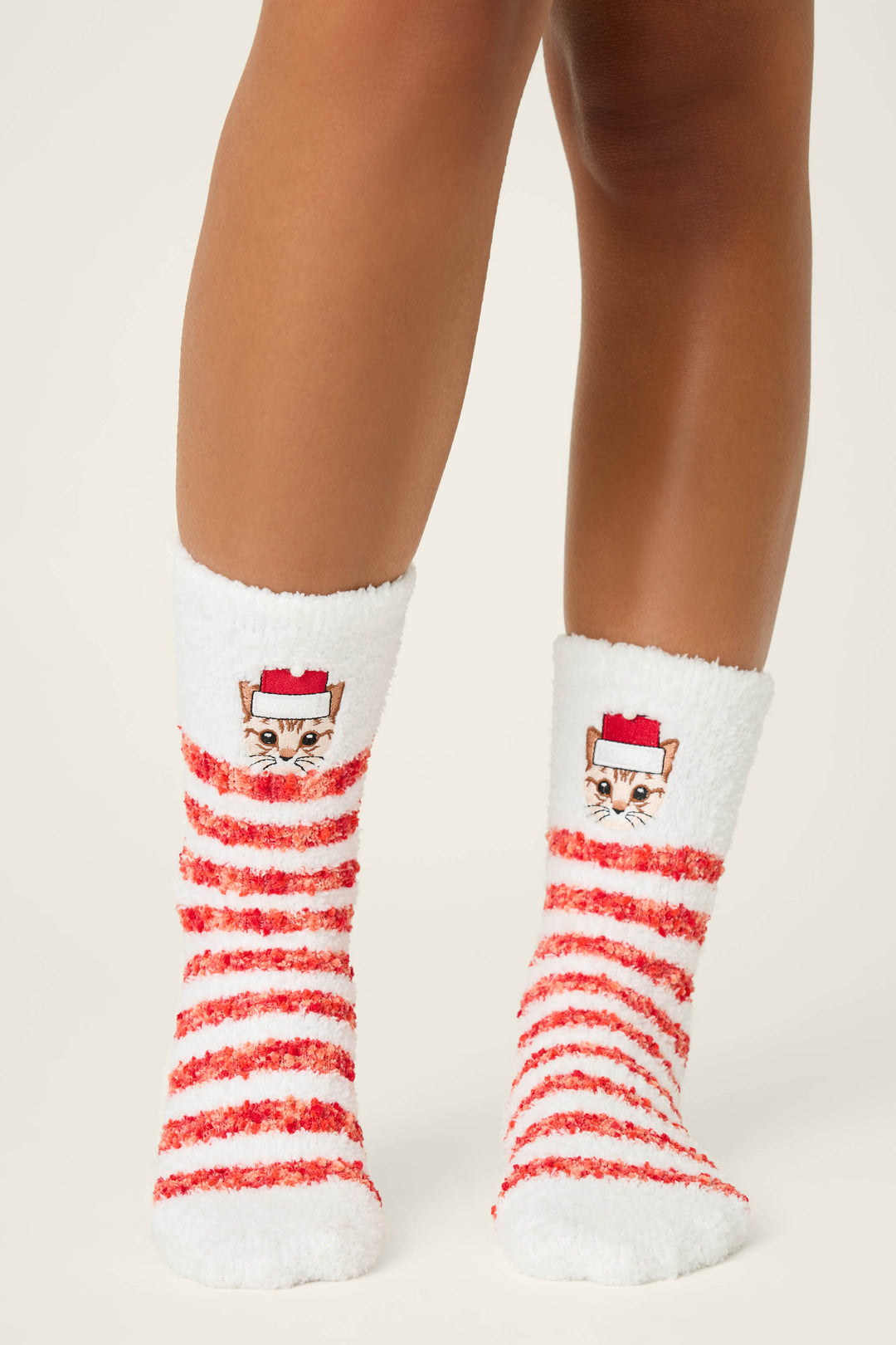 Someone wears P.J. Salvage CAT SOCKS FELINE FESTIVE—fuzzy white socks with red stripes and a cat face in a red hat near the top—displayed against a plain light background.