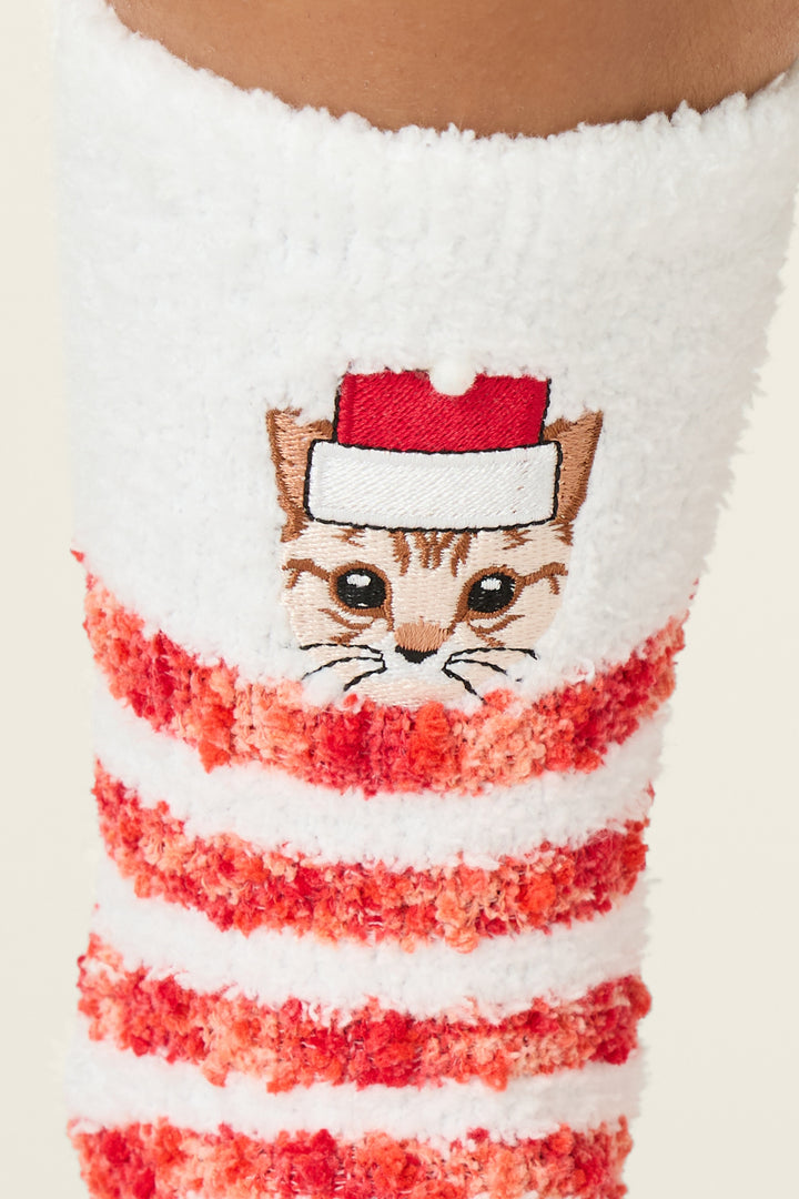 A close-up of P.J. Salvage's Feline Festive Cat Print Crew Socks with Grippers, showing a fuzzy white and red striped design, an embroidered cat face in a Santa hat, worn on a person's leg.