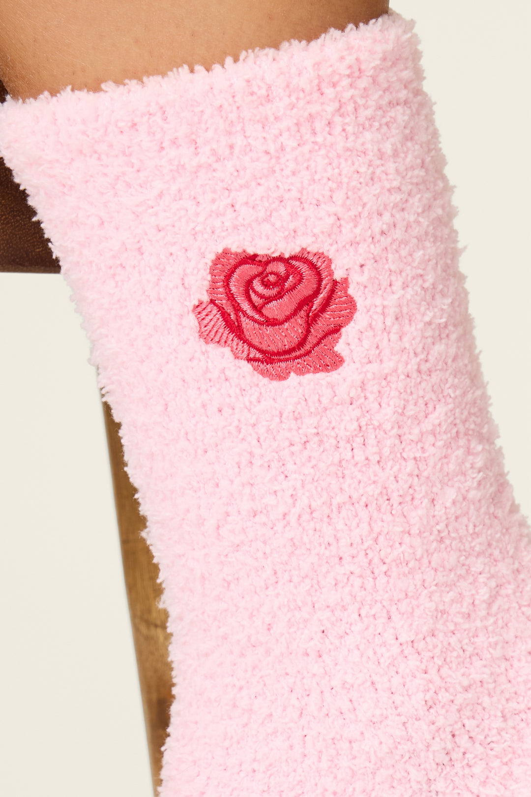 Close-up of P.J. Salvage Crazy For The Holidays Rose Crew Socks with Grippers in pink, featuring a red embroidered rose near the top. Shown against a neutral light background.