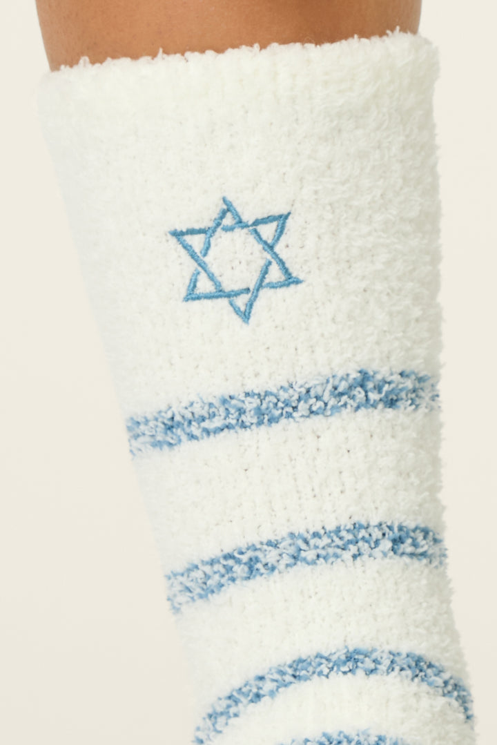 A close-up of the P.J. Salvage You Had Me At Shalom Crew Socks with Grippers, featuring white fuzzy fabric, blue horizontal stripes, and a blue embroidered Star of David near the top.
