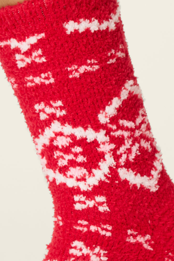 A close-up of the P.J. Salvage Crazy For The Holidays Fairisle Print Crew Socks with Grippers shows their soft, cozy texture and festive red design with white snowflakes. The plain background highlights the holiday look.