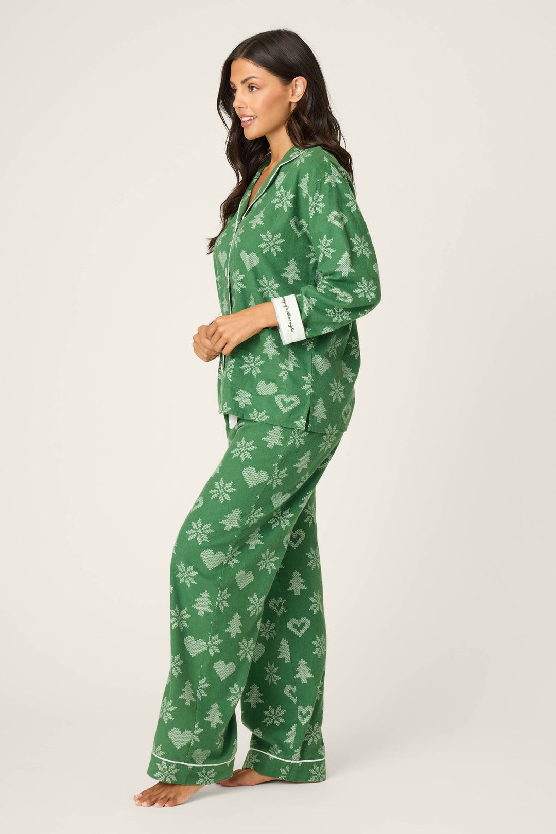 A woman stands barefoot in side profile, wearing the P.J. Salvage 4-Piece Tree & Heart Print Flannel PJ Set with white trim on the collar, cuffs, and pant legs. The background is plain and light-colored.