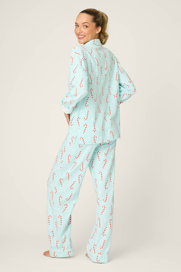 A person stands barefoot, facing away but smiling over their shoulder, wearing the P.J. Salvage 4-Piece Candy Cane Print Flannel PJ Set in light blue, against a plain beige background.