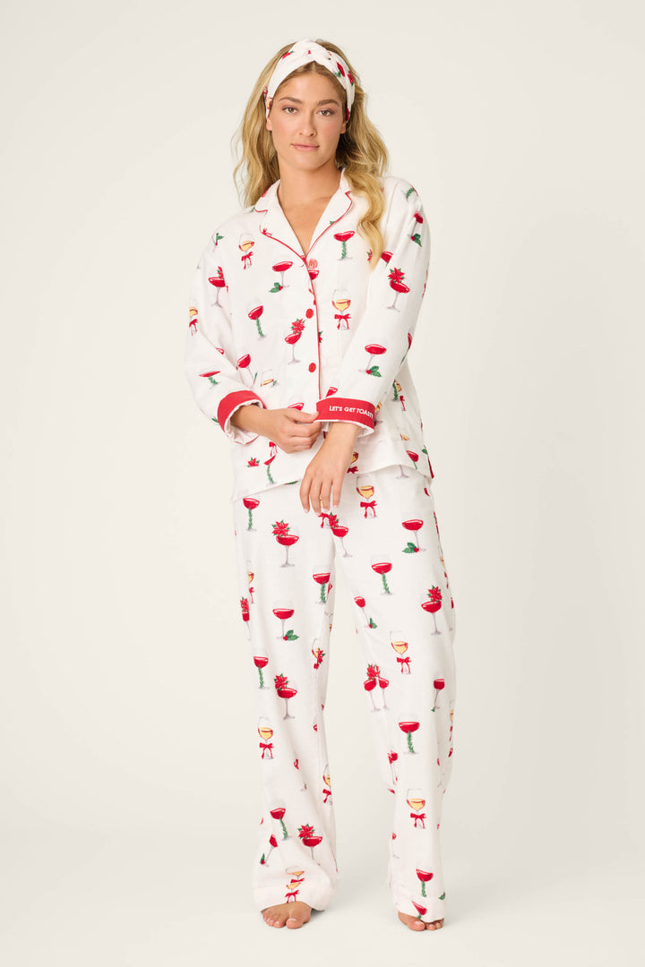 A woman wears the P.J. Salvage BEARS PJ SET FLANNELS, featuring white flannel pajamas with festive red and green drink and ornament prints, red-trimmed cuffs, and a matching headband. She stands barefoot facing forward against a plain background.