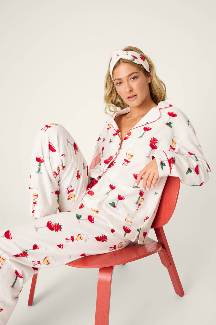 A person sits on a red chair wearing the BEARS PJ SET FLANNELS by P.J. Salvage, featuring white pajamas with a holiday print and a matching headband against a plain light background.