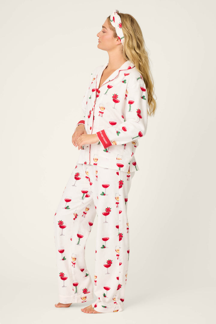 A person stands barefoot in the BEARS PJ SET FLANNELS by P.J. Salvage, featuring white pajamas and a matching headband with red and green drink glass prints, facing left with relaxed arms against a plain, light background.