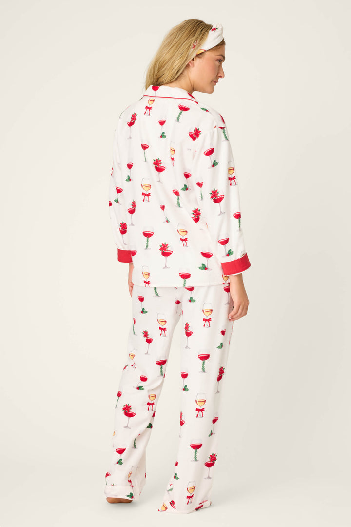 A person faces away, wearing the BEARS PJ SET FLANNELS by P.J. Salvage—white pajamas with red trim, festive cocktail prints, and a matching headband over blonde hair—set against a plain light background.