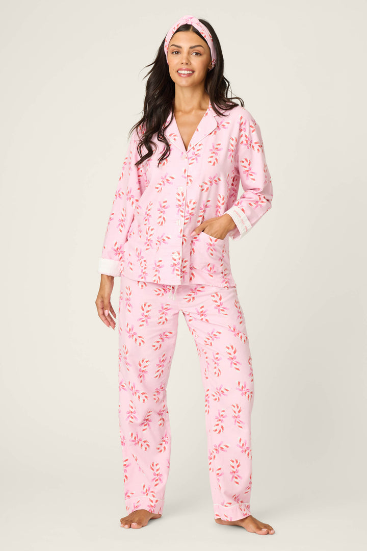 A woman smiles in the P.J. Salvage 3-Piece Candy Cane Print Flannel PJ Set, featuring a matching headband, with one hand in her pocket against a plain light background.