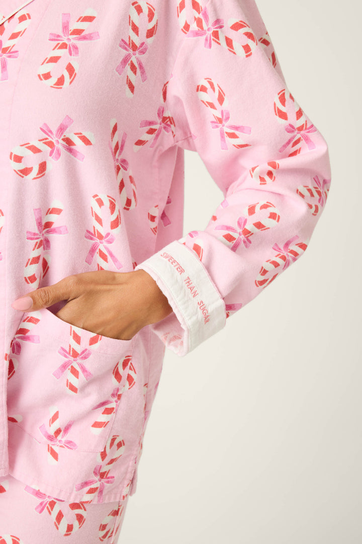 A person models the P.J. Salvage 3-Piece Candy Cane Print Plus Size Flannel PJ Set, featuring pink pajamas with red and white candy canes and a cuff that reads “SWEETER THAN SUGAR.”.