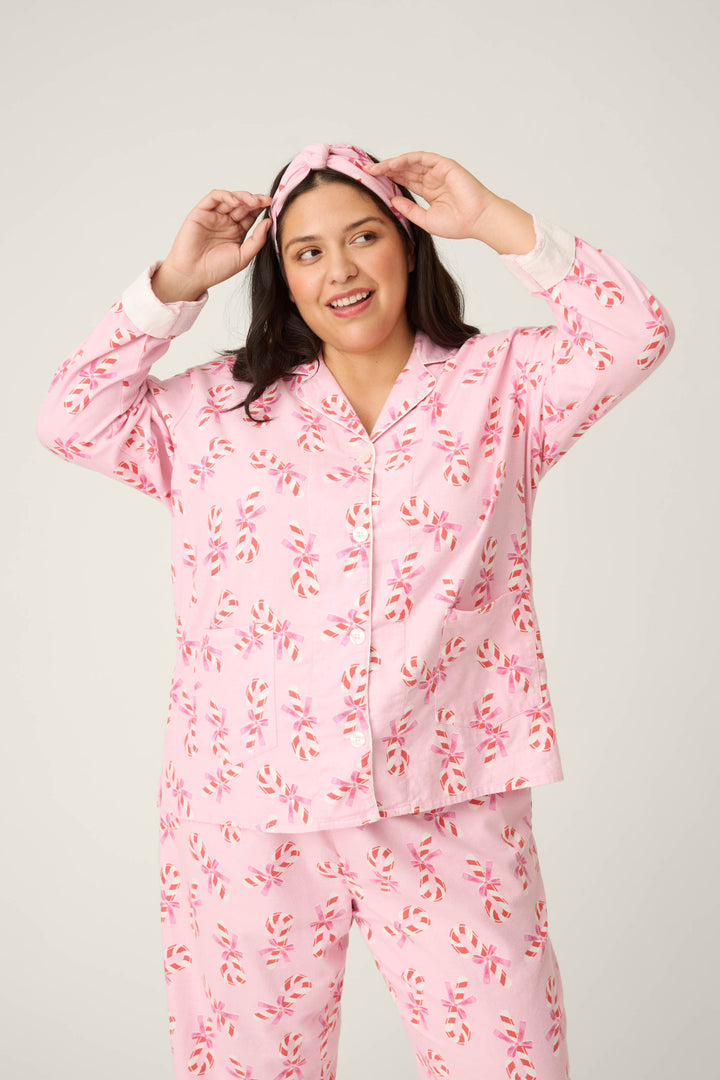A person smiles at the camera, adjusting their headband while wearing the P.J. Salvage 3-Piece Candy Cane Print Plus Size Flannel PJ Set against a plain background.