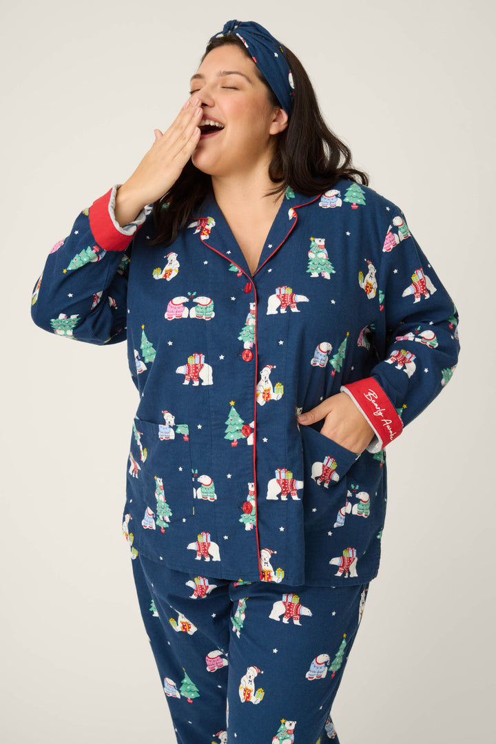 A woman, wearing the P.J. Salvage 3-Piece Bear Print Plus Size Flannel PJ Set with a matching headband, yawns with one hand covering her mouth and the other in her pocket.