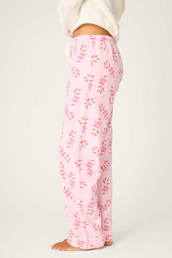 A person stands barefoot against a plain background, showing only their lower half while wearing P.J. Salvage Candy Cane Print Open Leg Flannel Pants in light pink with a red and white candy cane pattern.