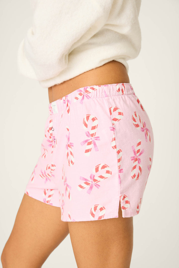 Model wears P.J. Salvage's Sweeter Than Sugar Candy Cane Print Flannel Shorts—pink cotton flannel pajama shorts with red and white candy canes—and a white fuzzy sweater, shown waist to mid-thigh on a plain background.