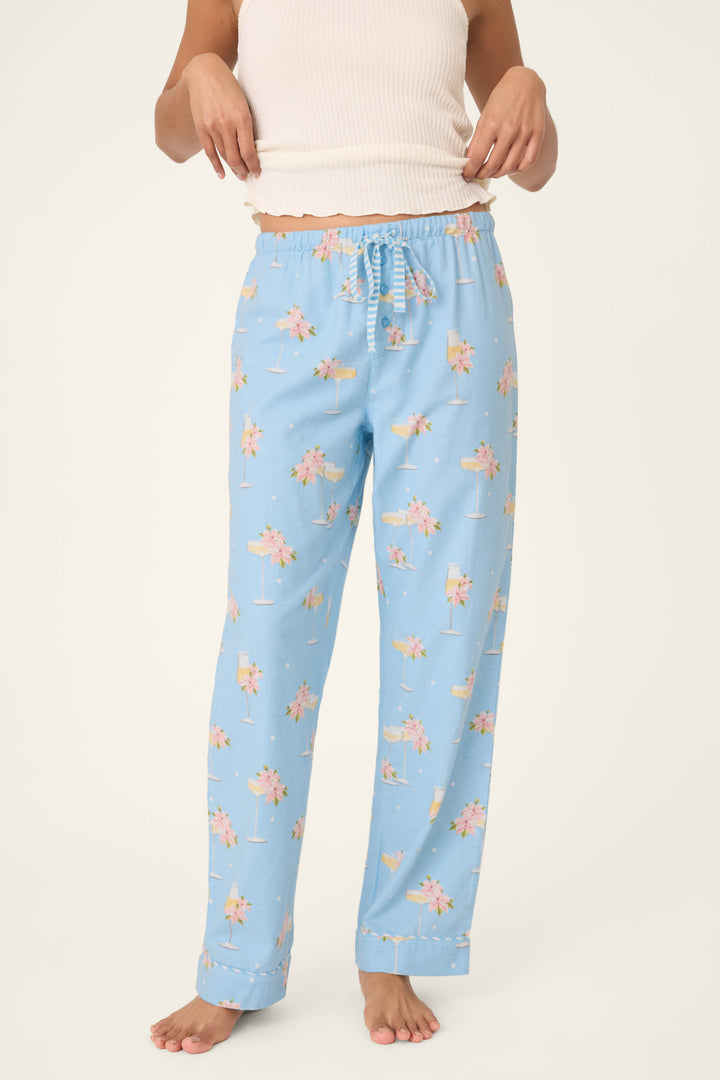 A person stands barefoot against a plain background, wearing P.J. Salvage's Fizz the Season Open Leg Flannel Pants in light blue with a pink floral pattern and a white sleeveless top, with their hands near the waistband.