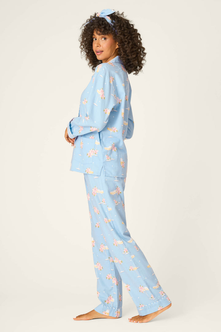 A person stands barefoot against a plain background, wearing the P.J. Salvage Fizz The Season 3-Piece Flannel PJ Set: a matching floral light blue pajama with long sleeves, full-length pants, and a coordinating headband.