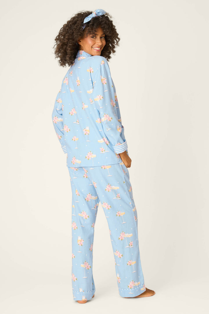 A person with curly hair poses barefoot against a plain background wearing the P.J. Salvage Fizz The Season 3-Piece Flannel PJ Set—a matching light blue pajama set and headband with a small pink and white floral pattern.